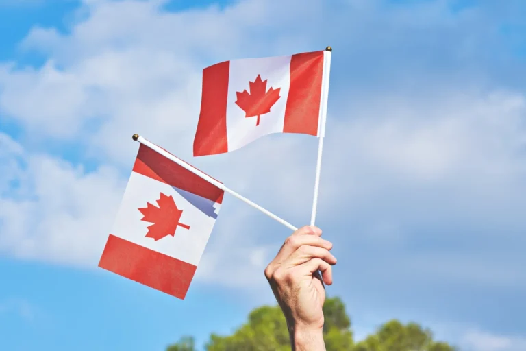 Raised hand with two waving Canadian flag against blue sky. Happy Canada day.